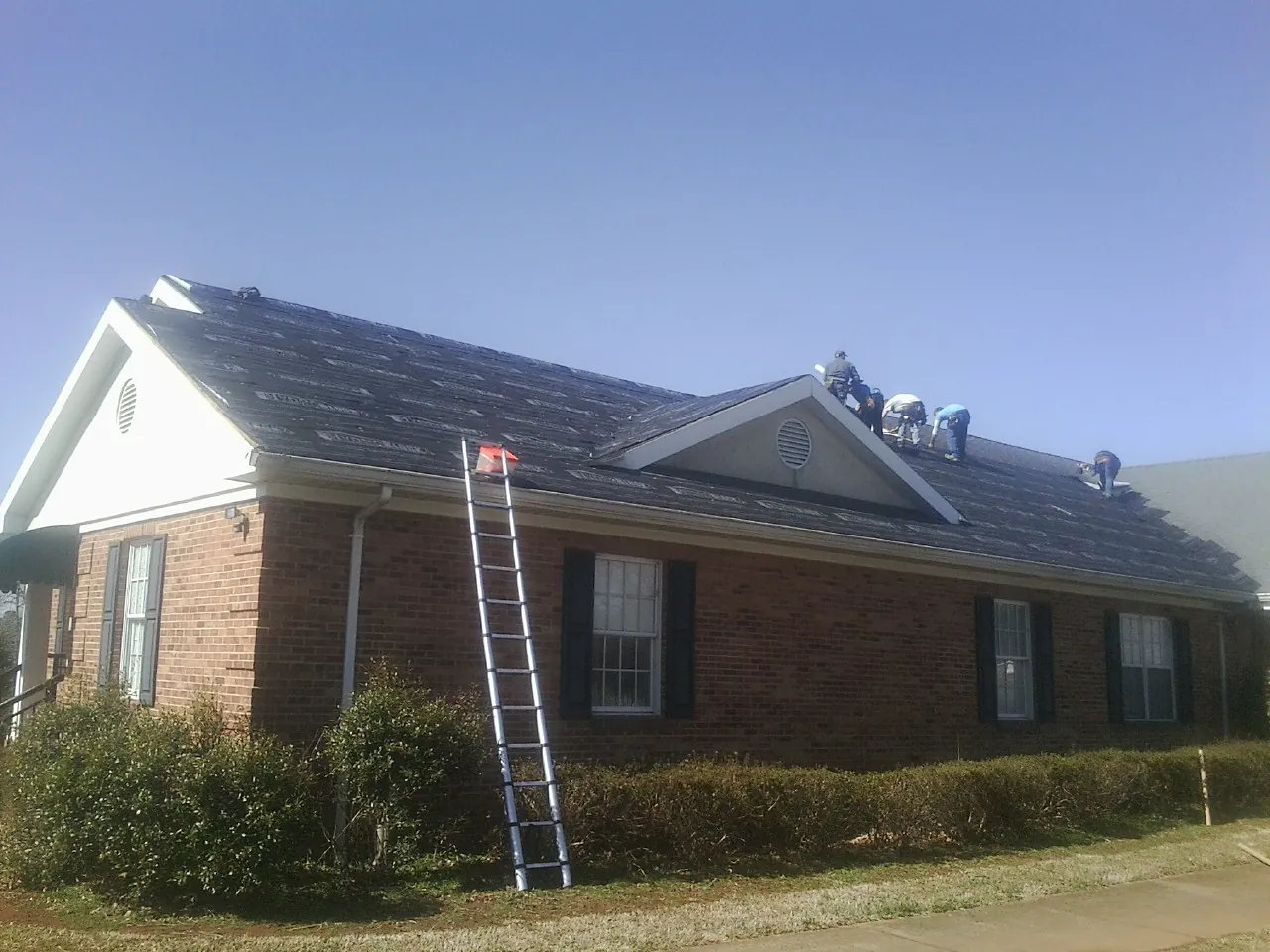 Crew tearing shingles off a brick ranch roof with a ladder set — Metal Roof Repair work by our crew in Peacham