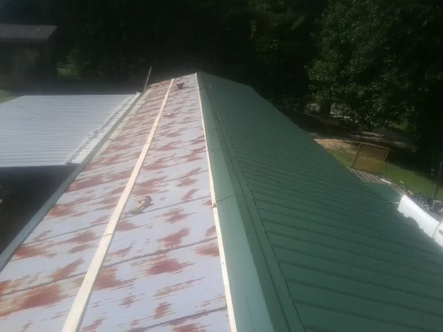 Old rusted panels beside newly installed green metal roofing — Wind Damage Roof Repair by Roofing Brothers in Peacham