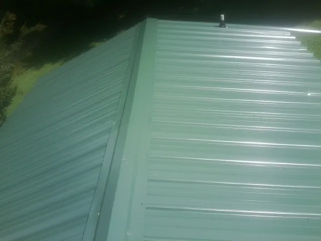 New green metal panels meeting at the ridge of a roof — Flat Roof Repair work by our crew in Peacham
