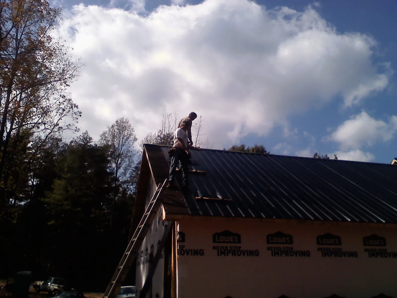 Roofer fastening dark metal panels high against a cloudy sky, from a Roof Inspection job in Peacham