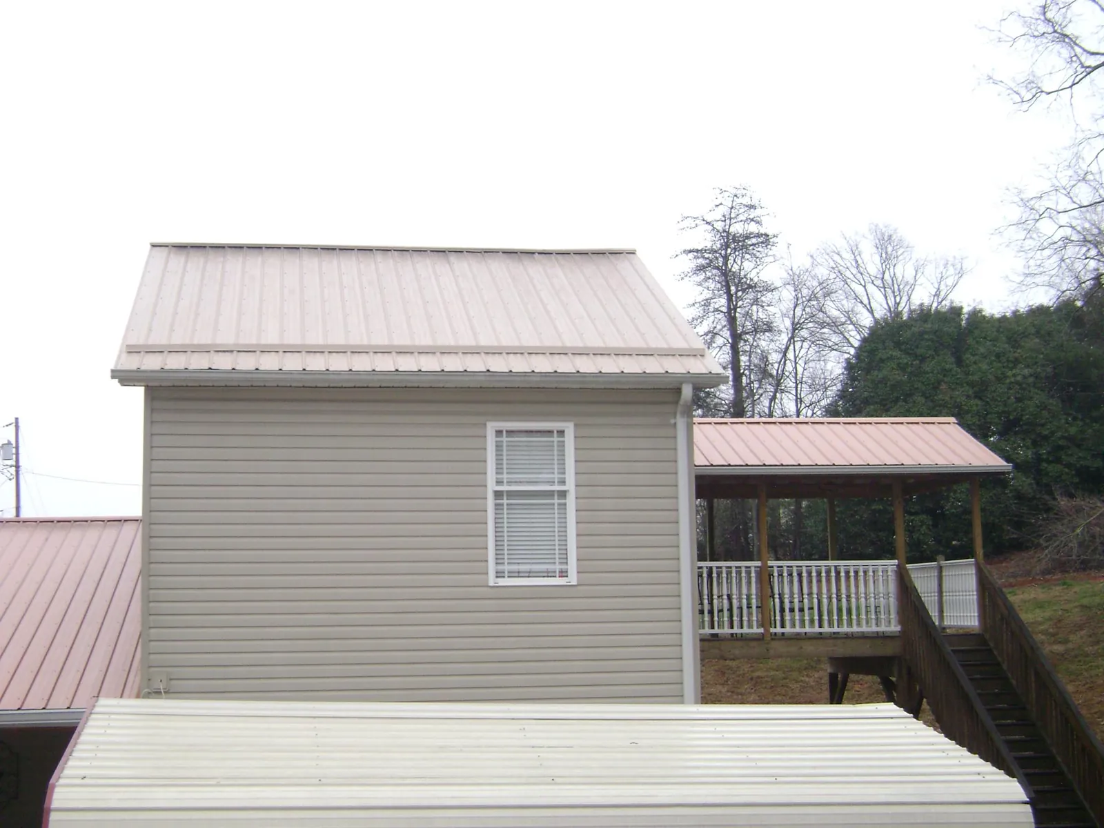 Tan metal roofs on a two story addition and attached porch, from a Roof Replacement job in Peacham